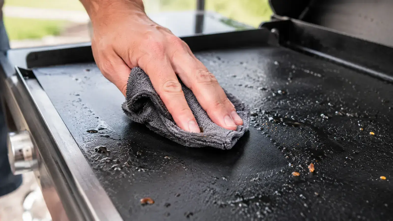 Grill mat being rinsed under a kitchen faucet with a sponge wiping it clean after a cook