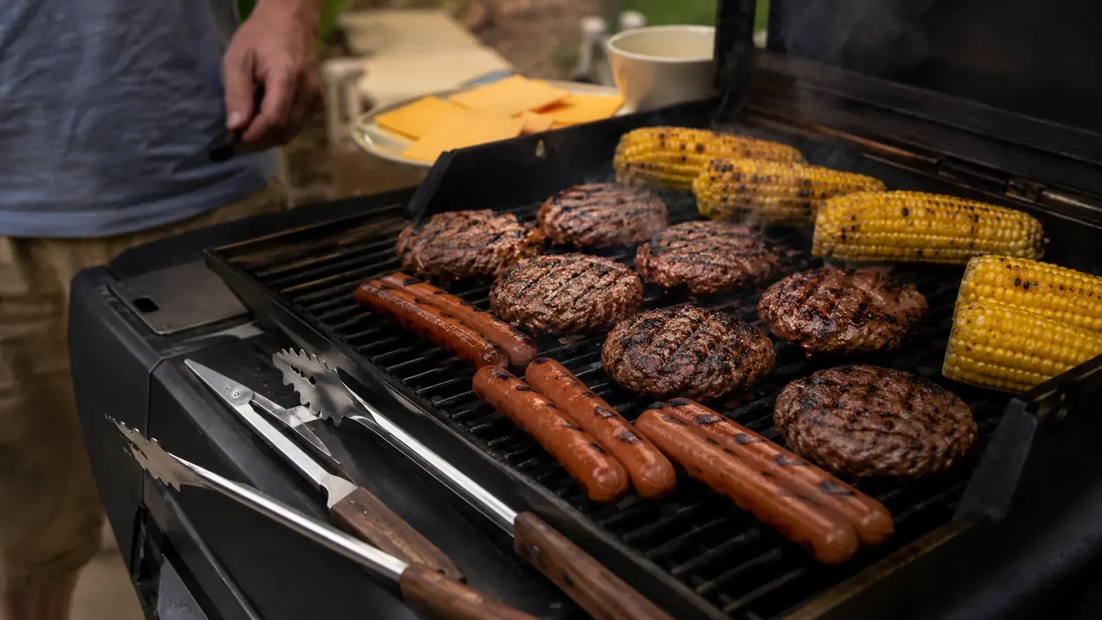 Close-up of a man's hand gripping a stainless steel barbecue tong with a thick rubber handle over glowing charcoal